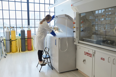 A lab technician standing over a piece of equipment, resembling a dryer, with a cloud of vapor coming out of it
